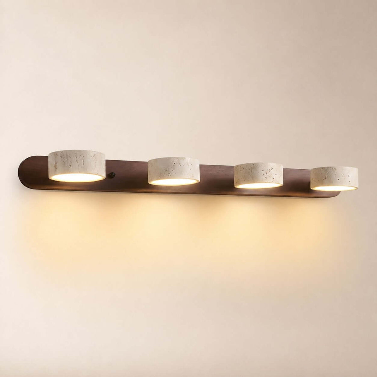 Avenor four-light vanity fixture with a walnut-finish wood backplate, round travertine shades, and a warm glow.