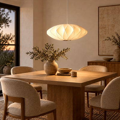 Corvya pendant light casting a warm glow over a rectangular wood dining table with upholstered chairs at dusk.