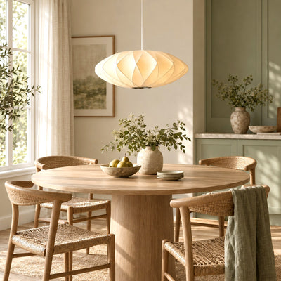 Corvya silk pendant light above a round wood dining table with woven chairs and sage green cabinets.