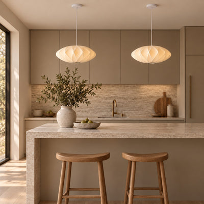 Two Corvya silk pendant lights above a stone kitchen island with wood stools and warm neutral cabinetry.