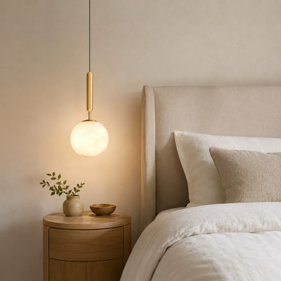 Small Velriq alabaster globe pendant light above a round nightstand beside a neutral bed